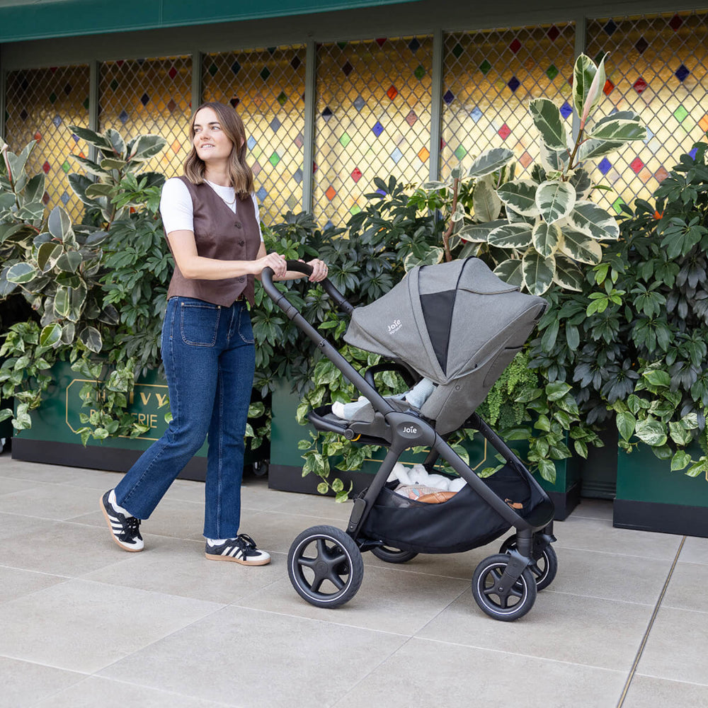 Woman pushing a Joie Finiti stroller with plants in the background