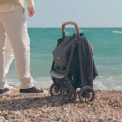 Black Joie Pact Pro lightweight compact pushchair, folded on beach